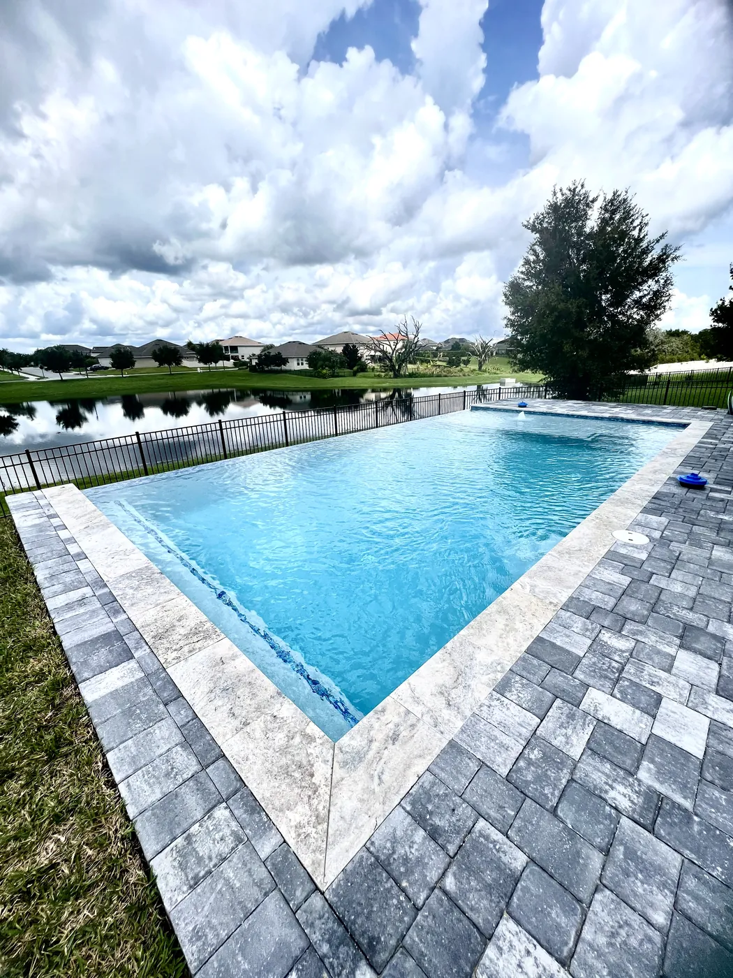 Finished pool with stone coping and gray pavers beside a lake